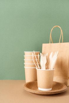 Reusable, disposable and recycling concept. Disposable eco friendly tableware on green background: paper bag, cups, forks and knives