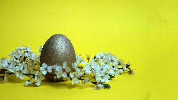 golden egg and flowering branch on yellow background, easter concept