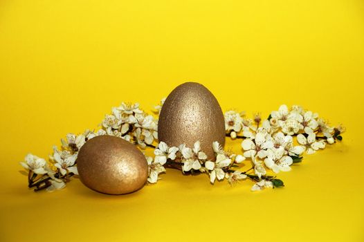 golden eggs and flowering branch on yellow background, easter concept