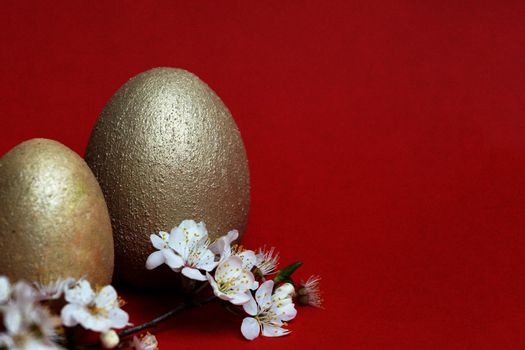 golden eggs and flowering branch on red background, easter concept, copy space