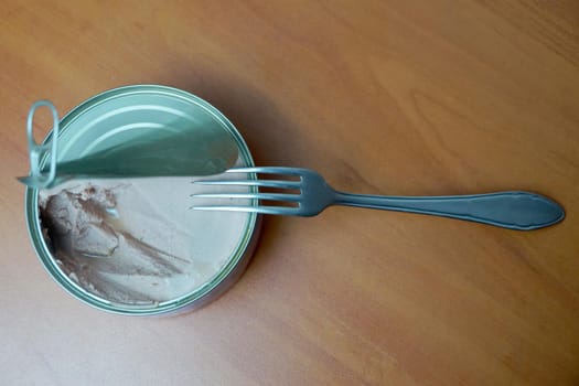 open tin can of pate and fork on wooden table.