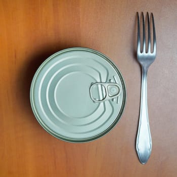 closed tin can and fork on wooden table.