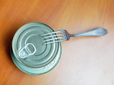 closed tin can and fork on wooden table.