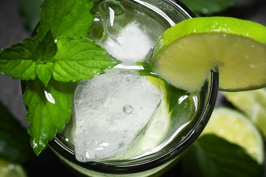 Fresh homemade mojito cocktail with lime, mint and ice on a black background, close-up.