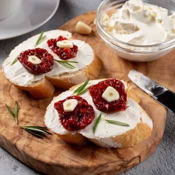 Homemade sandwiches with cream cheese and sun-dried tomatoes on a wooden board of olive - delicious healthy breakfast, italian cuisine, square image.