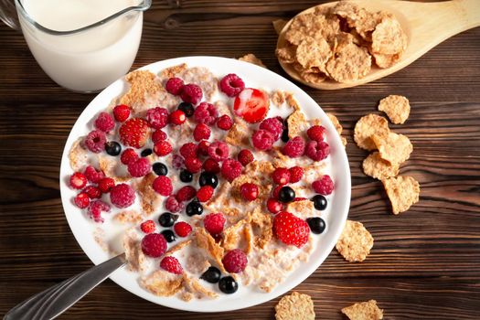 A bowl of cereal and berries with milk on a wooden table. Healthy summer breakfast.