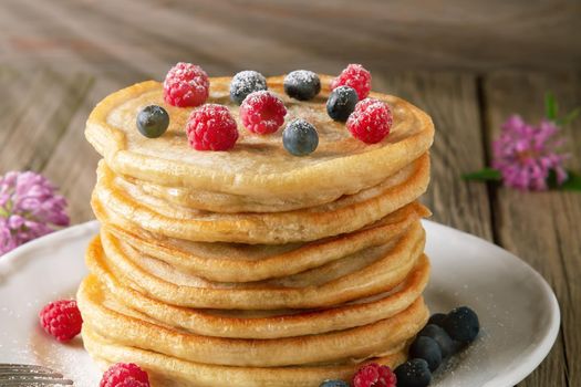 Stack of pancakes with fresh berries on a white plate on the table.