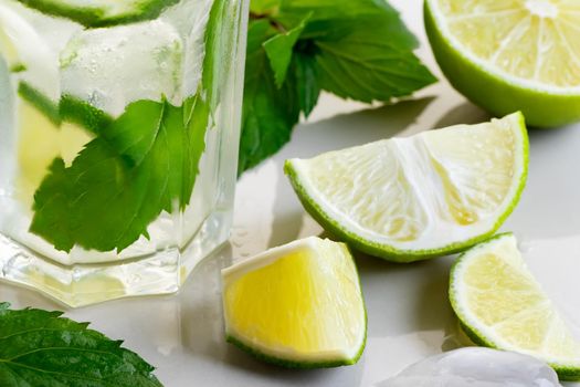 Fresh homemade cocktail with lime, mint and ice on a white table, close up.