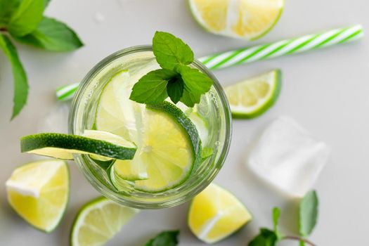 Fresh homemade cocktail with lime, mint and ice on a white table, close up, top view.
