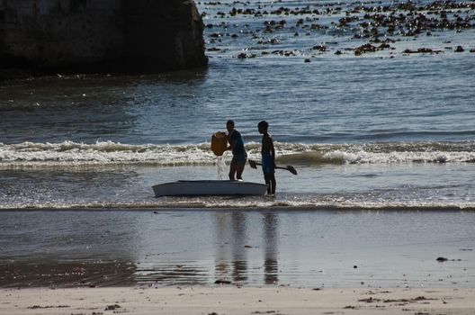 A candid shot of two boys playing with an old canoe in the surf a Hondeklip Bay. South Africa