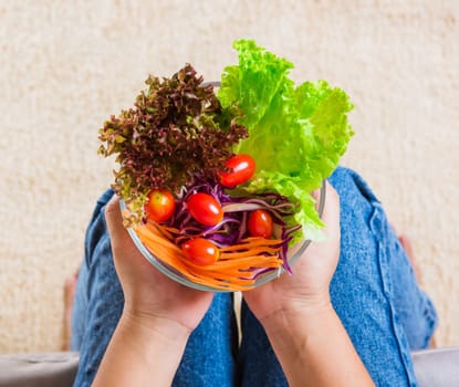 Top view of female hands holding bowl with green lettuce salad on legs, a young woman eating fresh salad meal vegetarian spinach in a bowl, Clean detox healthy food concept