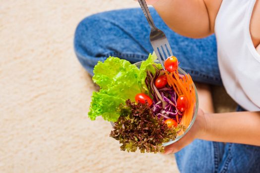 Top view of female hands holding bowl with green lettuce salad on legs, a young woman eating fresh salad meal vegetarian spinach in a bowl, Clean detox healthy food concept