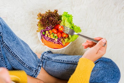 Female hands holding bowl with green lettuce salad on legs, Above young woman eating fresh salad meal vegetarian spinach in a bowl, Clean detox healthy homemade food concept