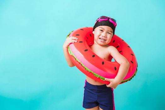 Summer vacation concept, Portrait Asian happy cute little child boy wear goggles and swimsuit hold watermelon inflatable ring, Kid having fun on summer vacation, studio shot isolated blue background