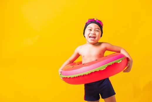 Summer vacation concept, Portrait Asian happy cute little child boy wear goggles and swimsuit hold watermelon inflatable ring, Kid having fun on summer vacation, studio shot isolated yellow background