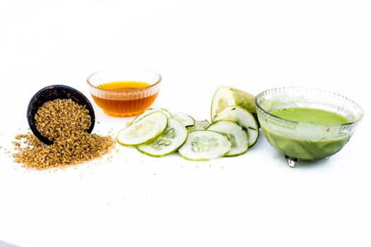 Cucumber face pack isolated on white i.e. Cucumber slices or cucumber pulp well mixed with turmeric powder and some lemon juice in a bowl and entire raw ingredients present on the surface.