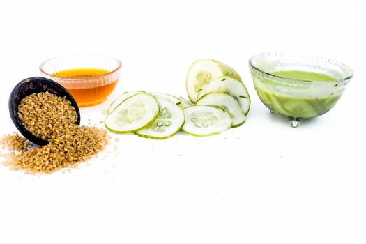 Cucumber face pack isolated on white i.e. Cucumber slices or cucumber pulp well mixed with turmeric powder and some lemon juice in a bowl and entire raw ingredients present on the surface.