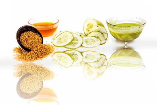Cucumber face pack isolated on white i.e. Cucumber slices or cucumber pulp well mixed with turmeric powder and some lemon juice in a bowl and entire raw ingredients present with their reflection also.