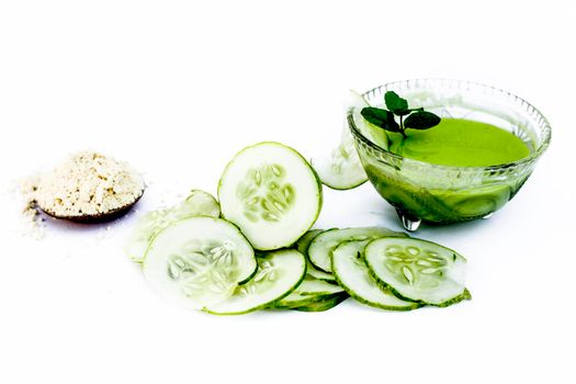 Cucumber face pack isolated on white i.e. Cucumber juice well mixed with gram flour in a glass bowl and all the raw ingredients present on the surface.Used for instant glow.