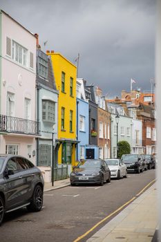 London, UK - February 14, 2020: Row of colorful British houses with cars parked outside. Beautiful English houses with bright colors and Victorian architecture. Peaceful London neighborhood