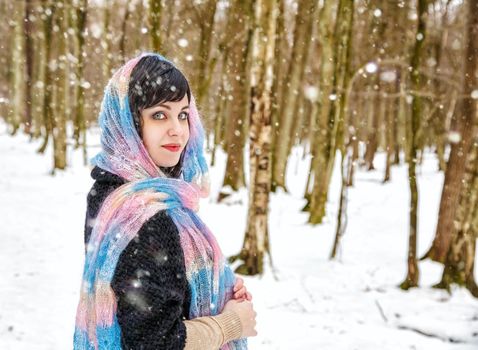 portrait of young beautiful woman walking under snowfall in the woods in winter 