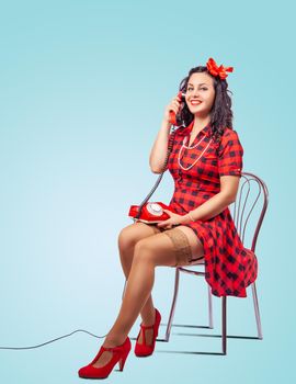 young beautiful woman speaks by phone while sitting on a chair in studio. pinup style