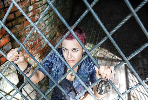 punk girl sitting on the floor behind metal bars in the dark room of hte abandoned castle closeup