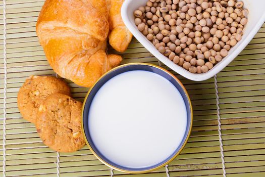 Milk in bowl with croissant baked bread, soy bean in cup on wooden bamboo and copy space for text. top view