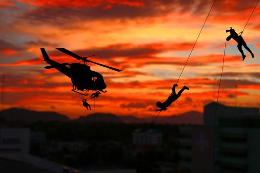 Silhouette Soldiers rappel down to attack from helicopter with sunset and copy space add text ( Concept stop hostilities To peace)