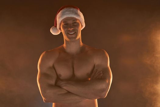 Portrait of muscular man wearing Christmas Santa hat, folded hands and smile on smoky background Macho Shirtless Naked torso stripper Hot sexy Santa guy Seductive male for holiday