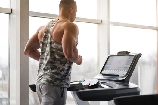 Muscular athletic bodybuilder fitness model running treadmill gym near big window jogging stationary machine do cardio training Weight loss Healthy lifestyle concept. Back view rear