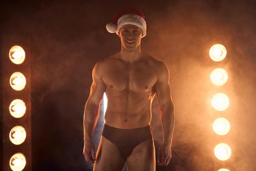 Portrait of muscular man wearing Christmas Santa hat, standing athletic pose on smoky background Macho Shirtless Naked torso stripper Hot sexy Santa guy Seductive male for holiday