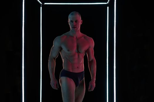 Active lifestyle concept. Professional bodybuilder showing perfect muscular body, neon lamps illumination on background Sport and fitness concept