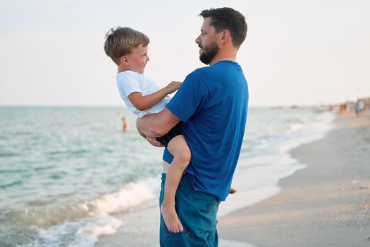 Father son spending time together sea vacation Young dad child little boy walking beach Fathers day. Family with one child. Happy childhood with daddy. sitting on hands laughs