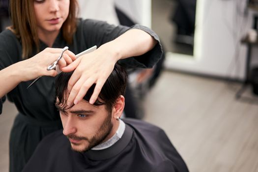 Stylish man sitting barber shop Hairstylist Hairdresser Woman cutting his hair Portrait handsome happy young bearded caucasian guy getting trendy haircut Attractive barber girl working serving client