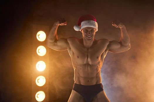 Portrait of muscular man wearing Christmas Santa hat, showing biceps muscle on smoky background Macho Shirtless Naked torso stripper Hot sexy Santa guy Seductive male for holiday