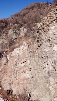 A group of people are engaged in rock climbing. High steep cliff. With the help of a rope, insurance and a partner, climbers climb to the top. Winter time of the year, sometimes there is snow.