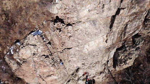 A group of people are engaged in rock climbing. High steep cliff. With the help of a rope, insurance and a partner, climbers climb to the top. Winter time of the year, sometimes there is snow.