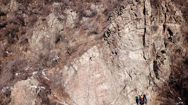 A group of people are engaged in rock climbing. High steep cliff. With the help of a rope, insurance and a partner, climbers climb to the top. Winter time of the year, sometimes there is snow.