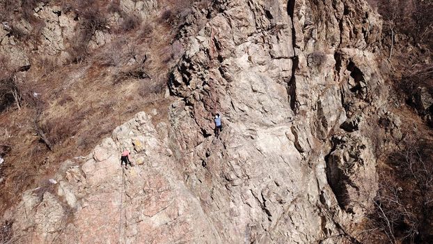 A group of people are engaged in rock climbing. High steep cliff. With the help of a rope, insurance and a partner, climbers climb to the top. Winter time of the year, sometimes there is snow.