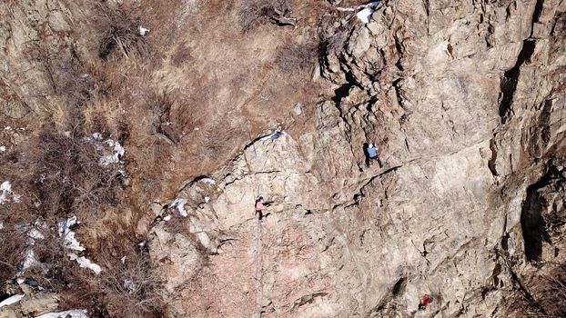 A group of people are engaged in rock climbing. High steep cliff. With the help of a rope, insurance and a partner, climbers climb to the top. Winter time of the year, sometimes there is snow.