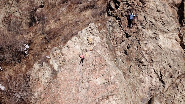 A group of people are engaged in rock climbing. High steep cliff. With the help of a rope, insurance and a partner, climbers climb to the top. Winter time of the year, sometimes there is snow.