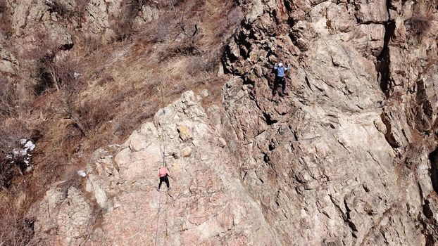 A group of people are engaged in rock climbing. High steep cliff. With the help of a rope, insurance and a partner, climbers climb to the top. Winter time of the year, sometimes there is snow.