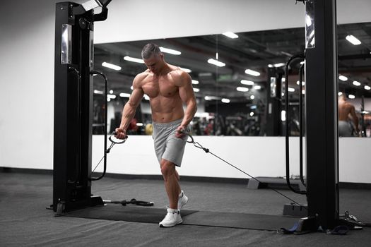 Muscular athletic bodybuilder standing training chest and shoulders muscles on fitness equipment wire cable machine Sport fitness healthy lifestyle Man do flyes exercises on gym machine