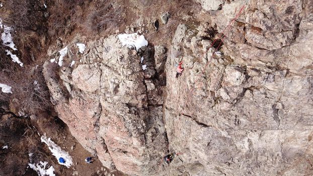 A group of people are engaged in rock climbing. High steep cliff. With the help of a rope, insurance and a partner, climbers climb to the top. Winter time of the year, sometimes there is snow.