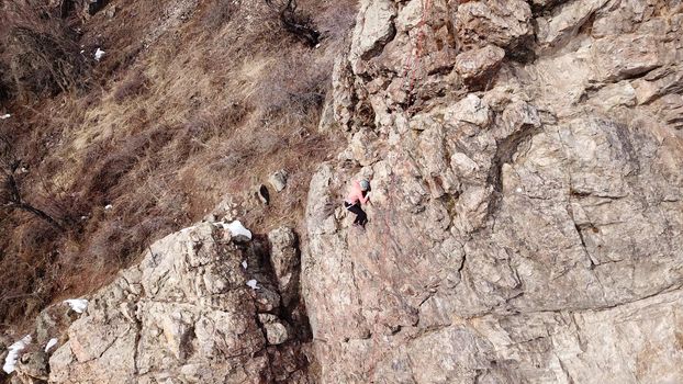 A group of people are engaged in rock climbing. High steep cliff. With the help of a rope, insurance and a partner, climbers climb to the top. Winter time of the year, sometimes there is snow.