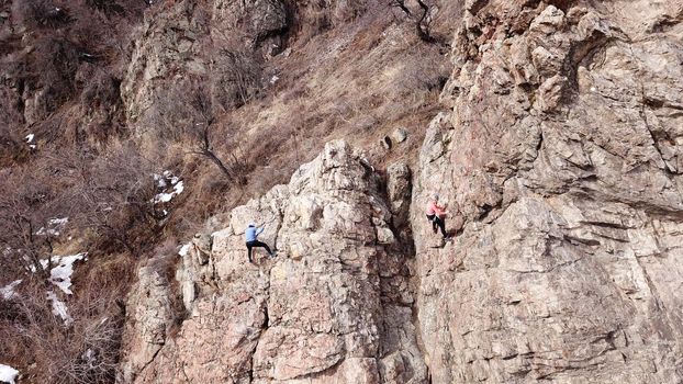 A group of people are engaged in rock climbing. High steep cliff. With the help of a rope, insurance and a partner, climbers climb to the top. Winter time of the year, sometimes there is snow.