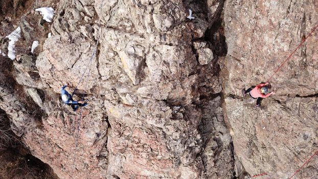 A group of people are engaged in rock climbing. High steep cliff. With the help of a rope, insurance and a partner, climbers climb to the top. Winter time of the year, sometimes there is snow.