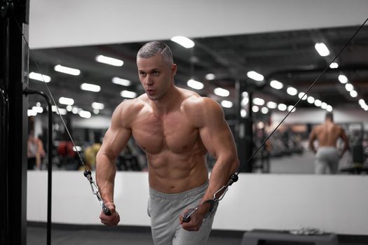Muscular athletic bodybuilder standing training chest and shoulders muscles on fitness equipment wire cable machine Sport fitness healthy lifestyle Man do flyes exercises on gym machine