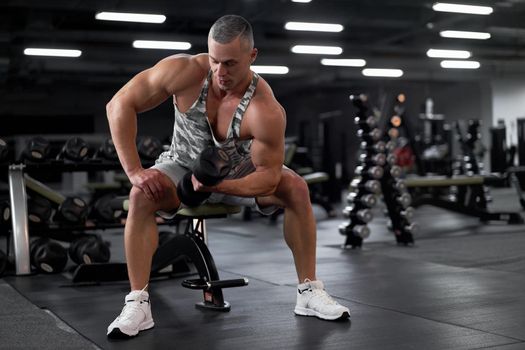 Muscular athletic bodybuilder fitness model sitting bench training biceps lift dumbbells through pain gym Sport fitness healthy lifestyle concept Caucasian person muscular body Functional training